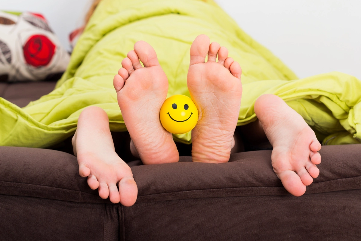 Two pairs of feet with a smiley face between them under a green blanket.
