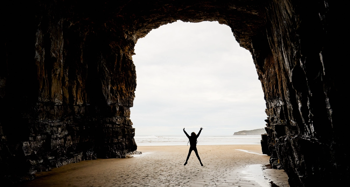 Person joyfully jumping inside a sea cave with an ocean view.