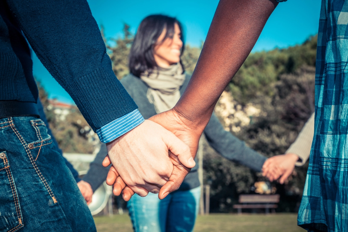People holding hands outdoors with a blurred background of a woman.