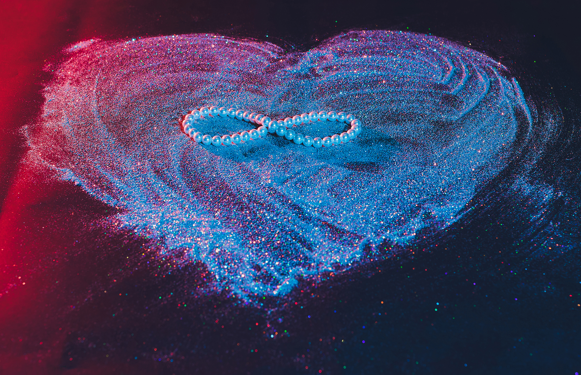 An infinity symbol shaped with glowing blue and pink powder on a dark surface.