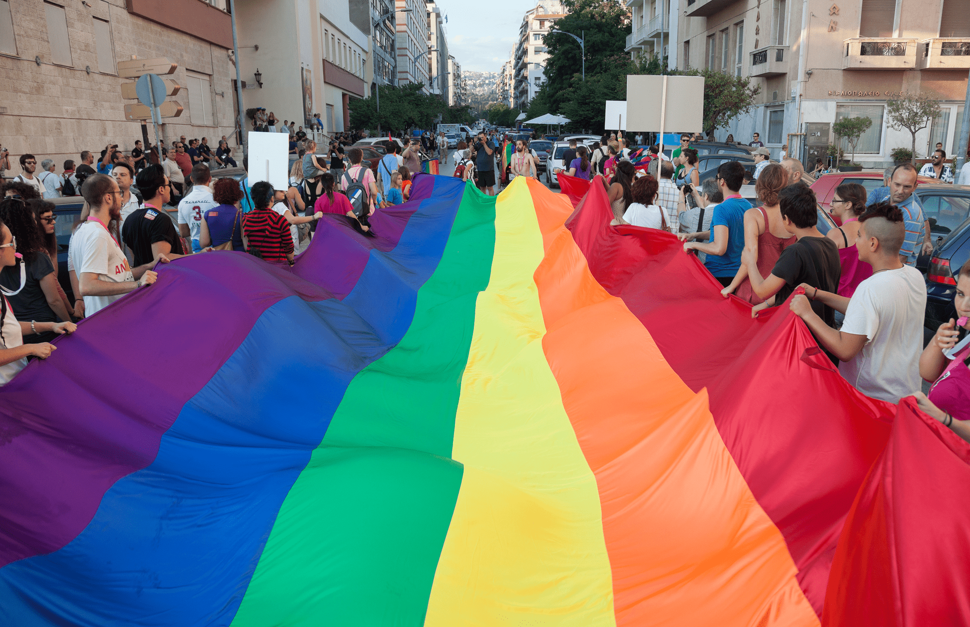 People holding a large rainbow pride flag in a street parade.