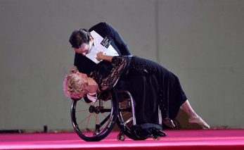 A man in a suit embraces a woman in a wheelchair on stage.